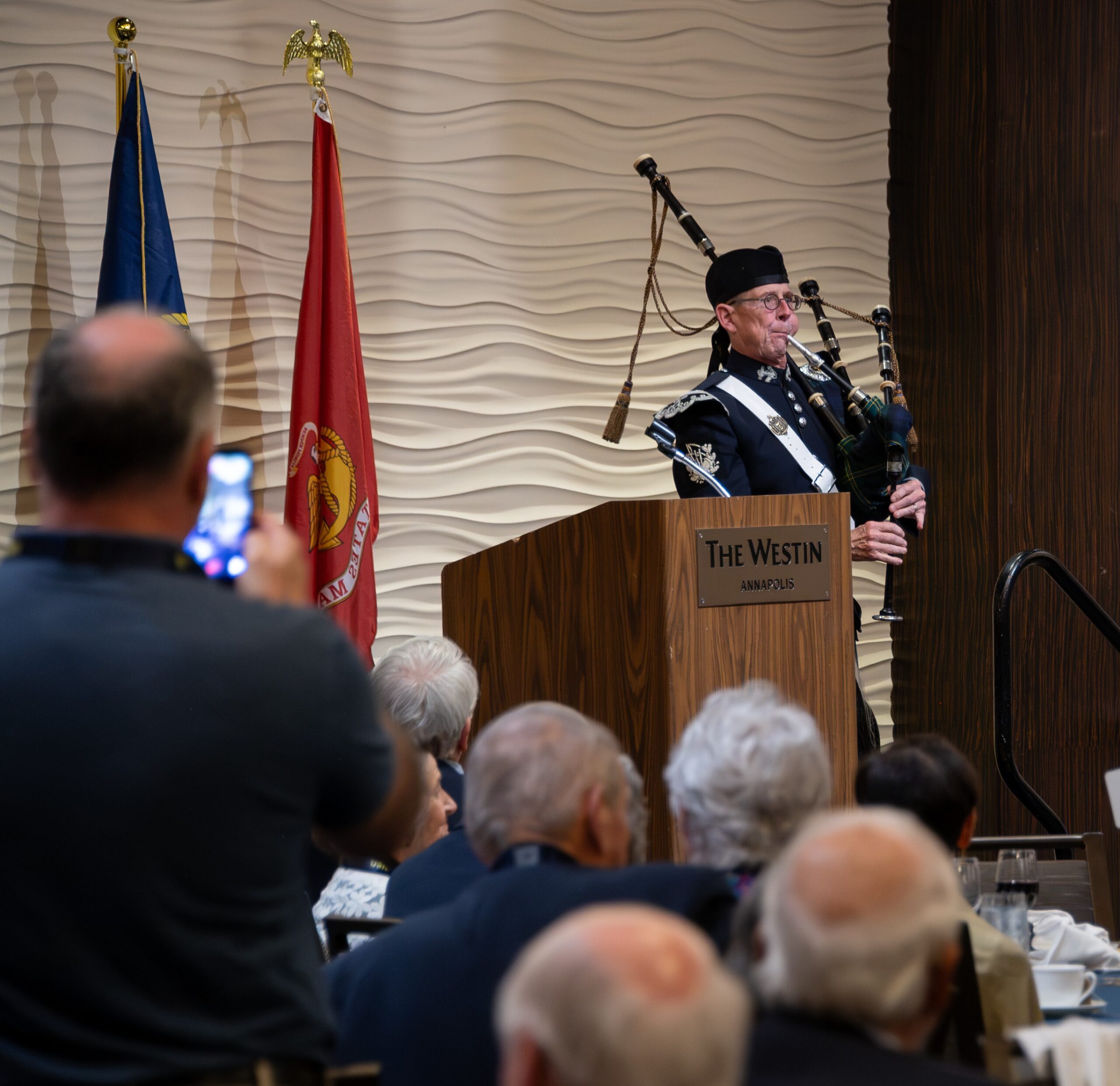 Bagpiper in dress uniform playing at the podium to welcome Classmates to the 60th Reunion banquet at The Westin Annapolis